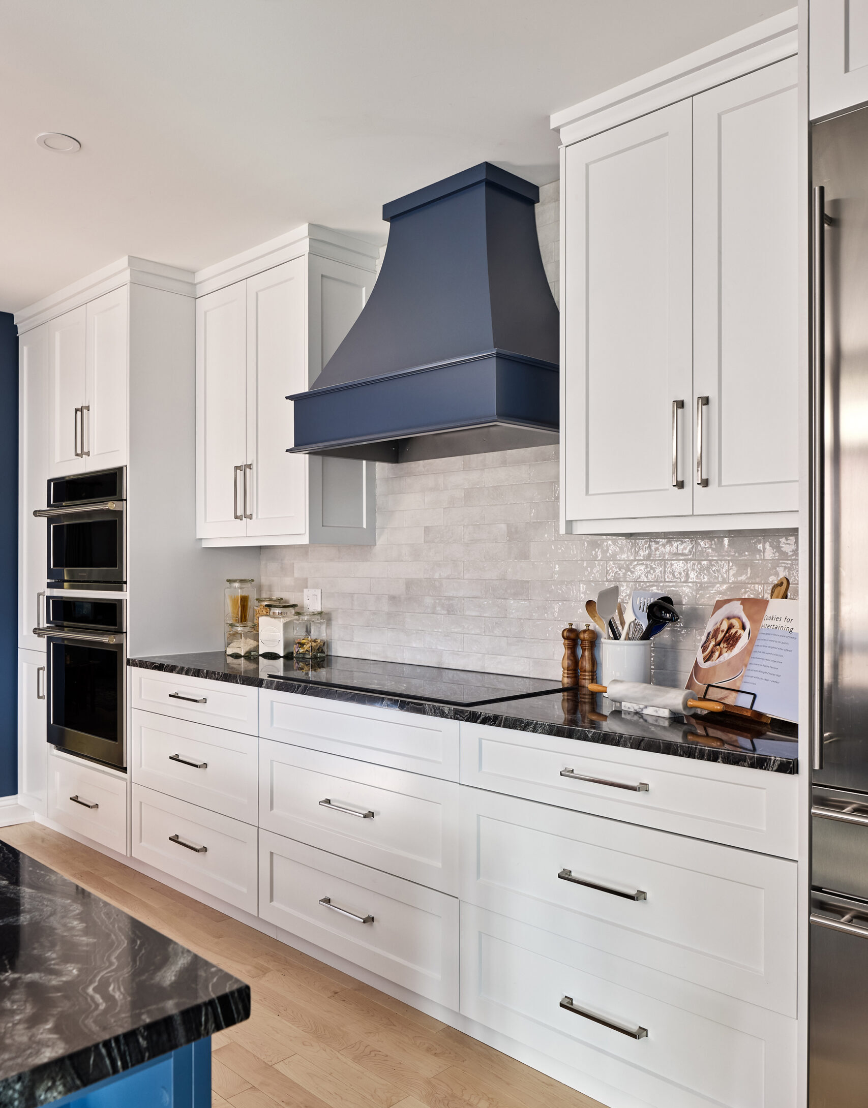 Transitional kitchen interior design with classic white cabinets and custom navy blue stove vent in West Orange.